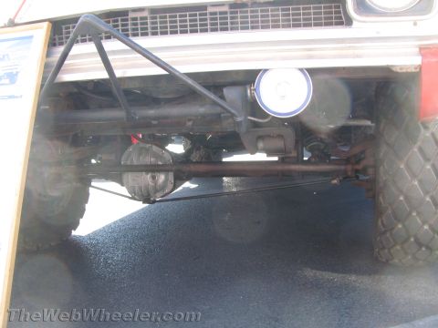 1990 Ford Bronco - low-angle view captures the front axle, leaf springs and steering linkage beneath a lifted off-road truck on pavement.