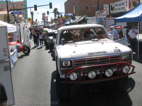 1990 Ford Bronco - white College of Southern Idaho off-road truck numbered 306 sits among a crowd of spectators and vendor tents on a sunny street.