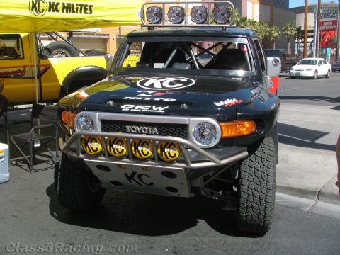 1990 Ford Bronco - black Toyota FJ Cruiser off-road race truck displayed at a street event, fitted with a KC HiLiTES roof light bar and yellow auxiliary light…