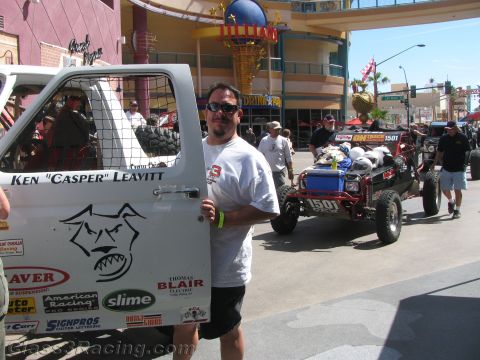 1990 Ford Bronco - man in sunglasses holds a white race truck door marked Ken Casper Leavitt on a sunlit casino street, with a number 1501 buggy behind.