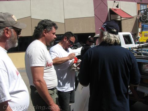 1990 Ford Bronco - group of men in t-shirts and ball caps gather and talk beside a white truck on a sunny street.