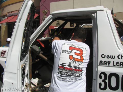 1990 Ford Bronco - man wearing a Class 3 Cup off-road racing t-shirt leans into the cab of a white number 300 race truck on a street.