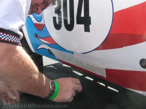1990 Ford Bronco - Close-up of a white race truck body panel marked number 304 with red and blue graphics, a man's wristbanded arm reaching below it.