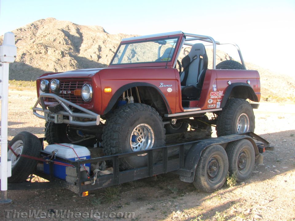 Red early Ford Bronco on a tandem-axle trailer in the desert