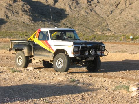 1990 Ford Bronco - 1970s-era Ford stepside pickup with white-and-black body, red and yellow side stripes and a front brush guard sits on a rocky desert trail.