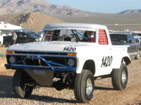 1990 Ford Bronco - white 1970s Ford pickup converted to a race truck, numbered 1420 with a tubular front end and racing seat, sits on a desert lot.