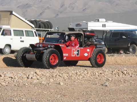 1990 Ford Bronco - Red open-cockpit desert race buggy with Hurst and Bilstein graphics and paddle tires, driven on a dirt lot with RVs behind.