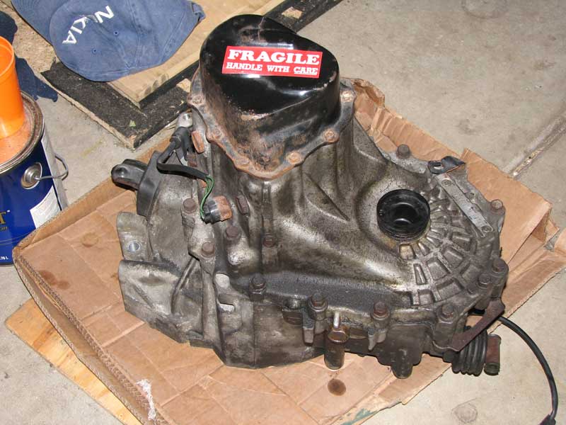 car transmission with 'FRAGILE HANDLE WITH CARE' sticker on top, sitting on cardboard