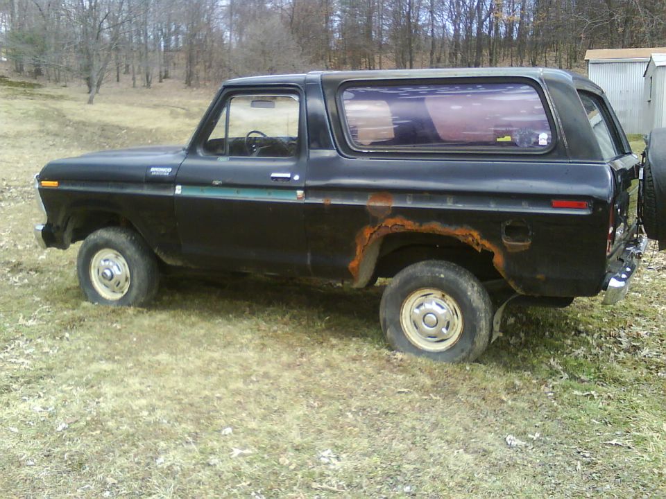 Side view of a black 1979 Ford Bronco with rusty wheel wells and flat tires