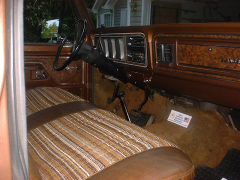 1978 Ford Bronco - The interior of a 1978 Ford Bronco shows its distinctive striped bench seat and woodgrain dashboard accents.