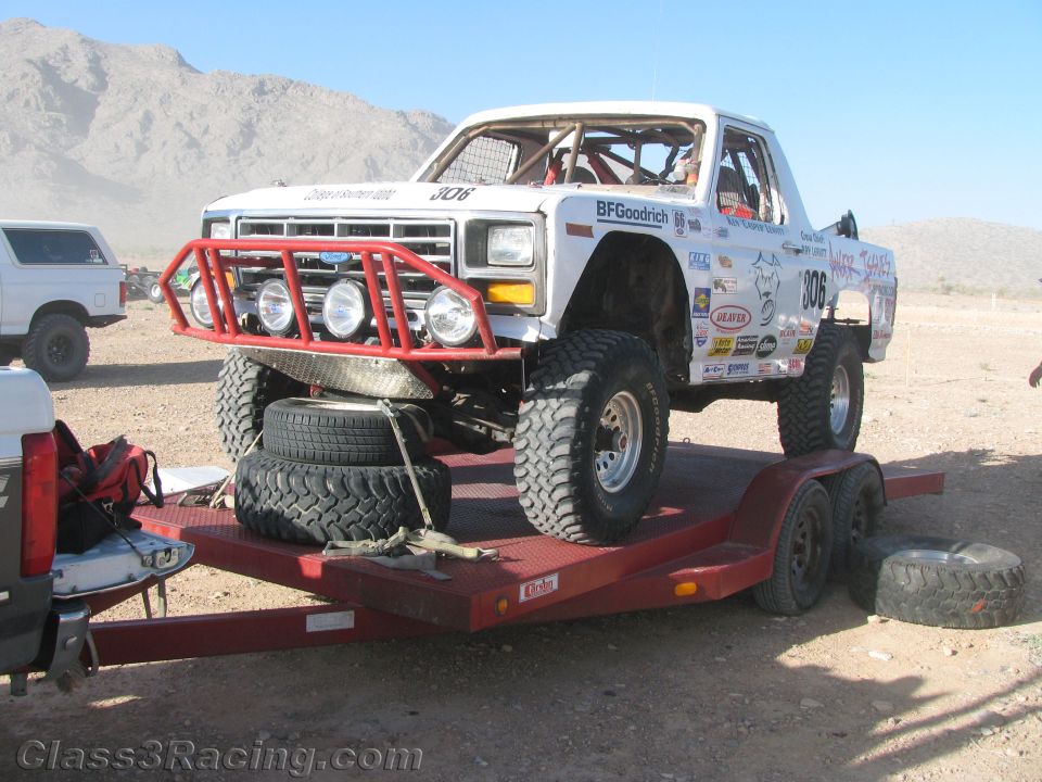 White vintage Ford race pickup number 306 with red brush guard strapped on a flatbed trailer