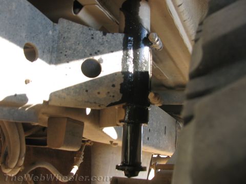 1990 Ford Bronco - Close-up underbody view of a black hydraulic shock absorber bolted to a light-colored frame next to a tire.