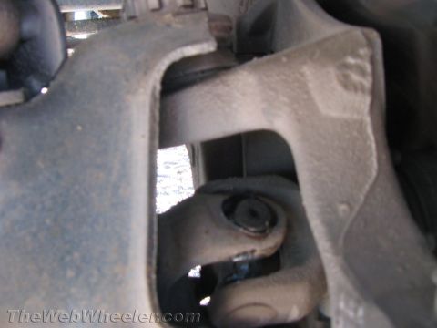 1990 Ford Bronco - Close-up underbody view of a steering shaft universal joint connecting to a cast steering knuckle on a vehicle's front end.