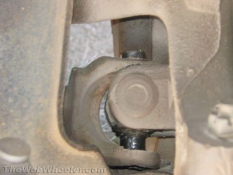1990 Ford Bronco - Detailed close-up of a steering shaft U-joint and yoke mounted to a firewall bracket under a vehicle.