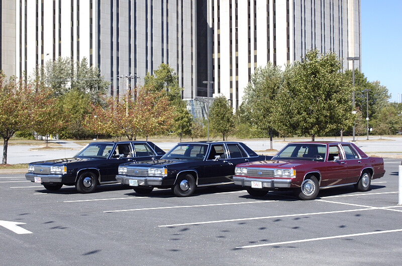 Three full-size sedans, two dark and one maroon, parked in a lot