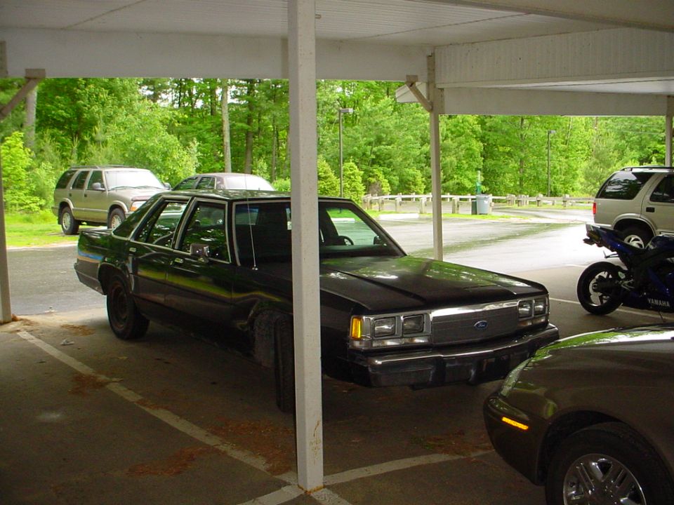 Black Ford sedan parked under a carport, 3/4 front view