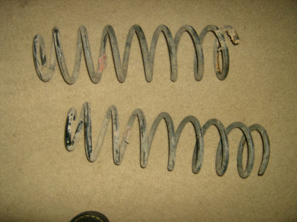 Two dirty, gray coil springs on a tan surface. One spring has a small red mark and a broken end