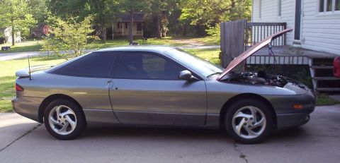 1995 Ford Probe - A gray 1995 Ford Probe coupe is parked outside a house with its hood open, revealing the engine bay.