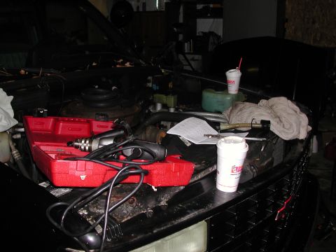 1999 Ford F-250 - The engine bay of a vehicle is open, with tools and coffee cups present, suggesting maintenance or repair work.