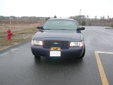 1999 Ford Crown Victoria - A dark blue Ford Crown Victoria is parked on a wet road in front of a fire hydrant.