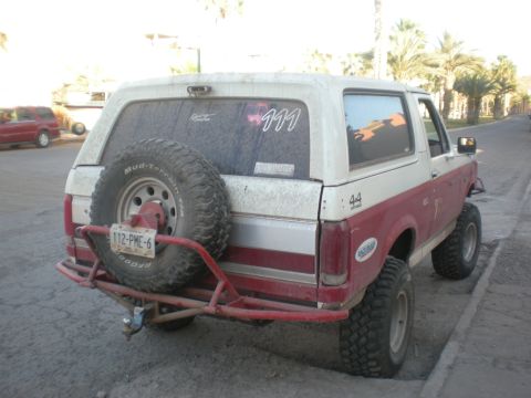 1993 Ford Bronco - This 1993 Ford Bronco features a two-tone red and white paint scheme and a rear-mounted spare tire with a custom bumper.