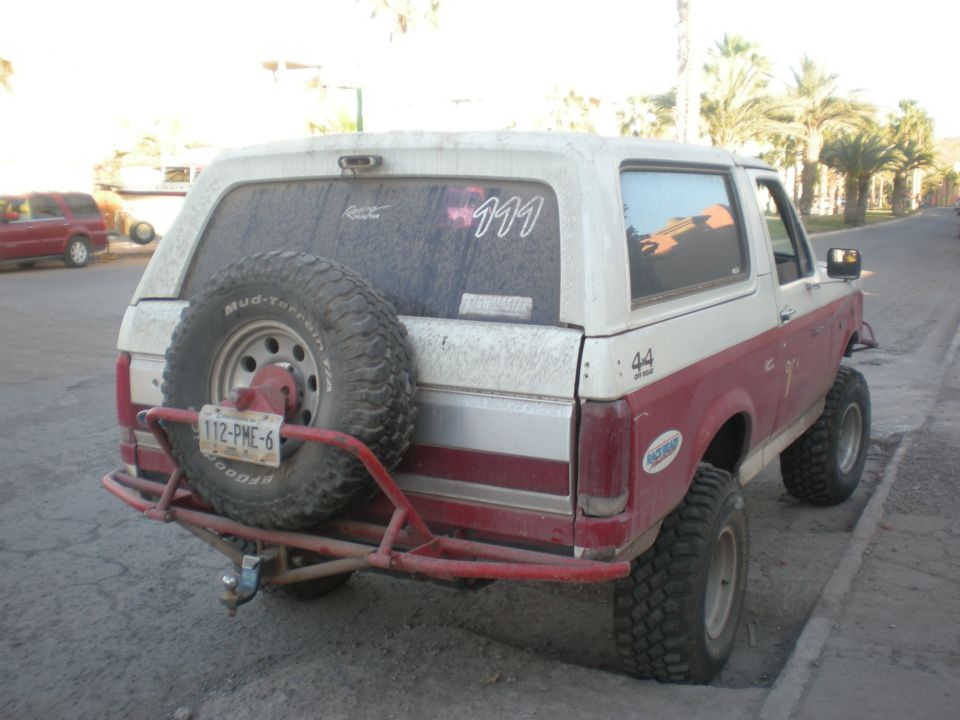 Red and white 1993 Ford Bronco rear view with spare tire and custom bumper