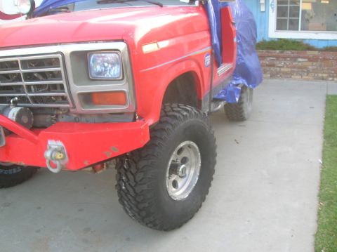 1985 Ford Bronco - This red pickup truck features a prominent grille and bumper, with a portion covered by a blue tarp.