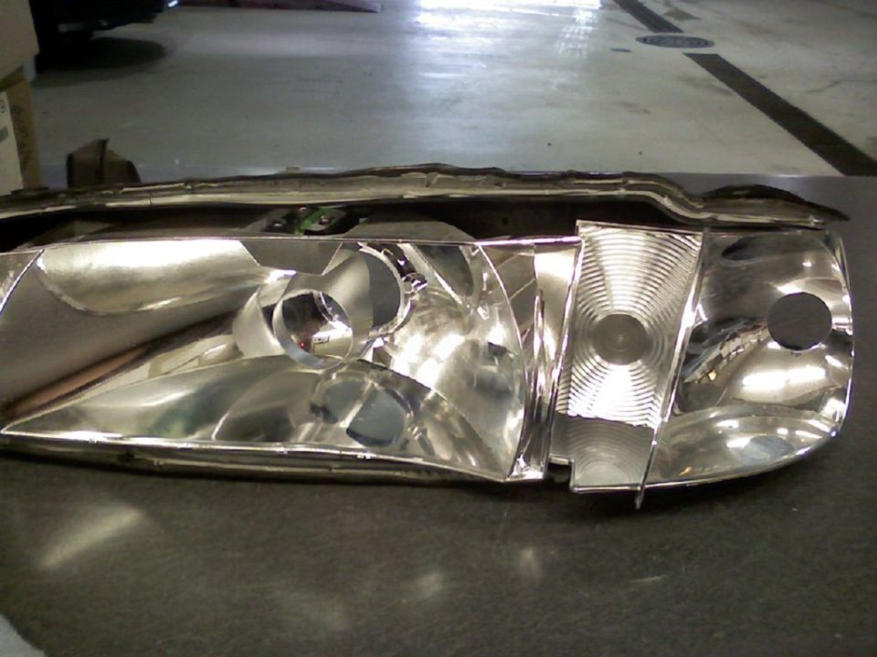 Headlight housing with lens removed showing bare chrome reflectors on a shop floor