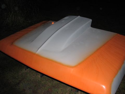 1979 Ford Bronco - A removed cowl-induction hood sits face-up on stands in the grass at night, mid-paint: the raised center scoop and surrounding panel are st…