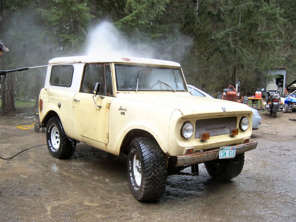 Cream International Scout SUV being pressure-washed on muddy lot, front 3/4 passenger view