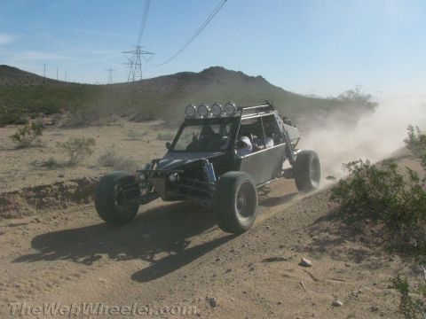 1990 Ford Bronco - black-and-silver tube-frame off-road buggy with roof-mounted lights races up a sandy desert trail.