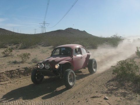 1990 Ford Bronco - maroon Baja-style off-road VW Beetle with off-road tires kicks up dust on a desert two-track.