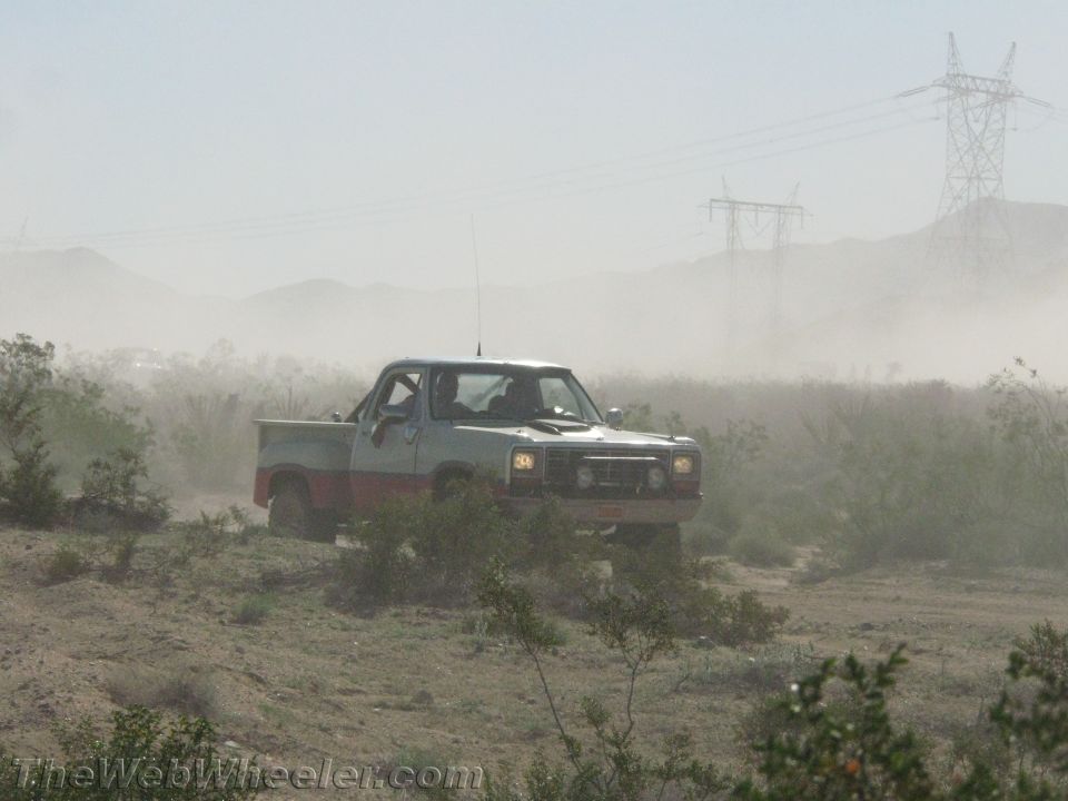 Older Dodge pickup truck driving through dusty desert brush