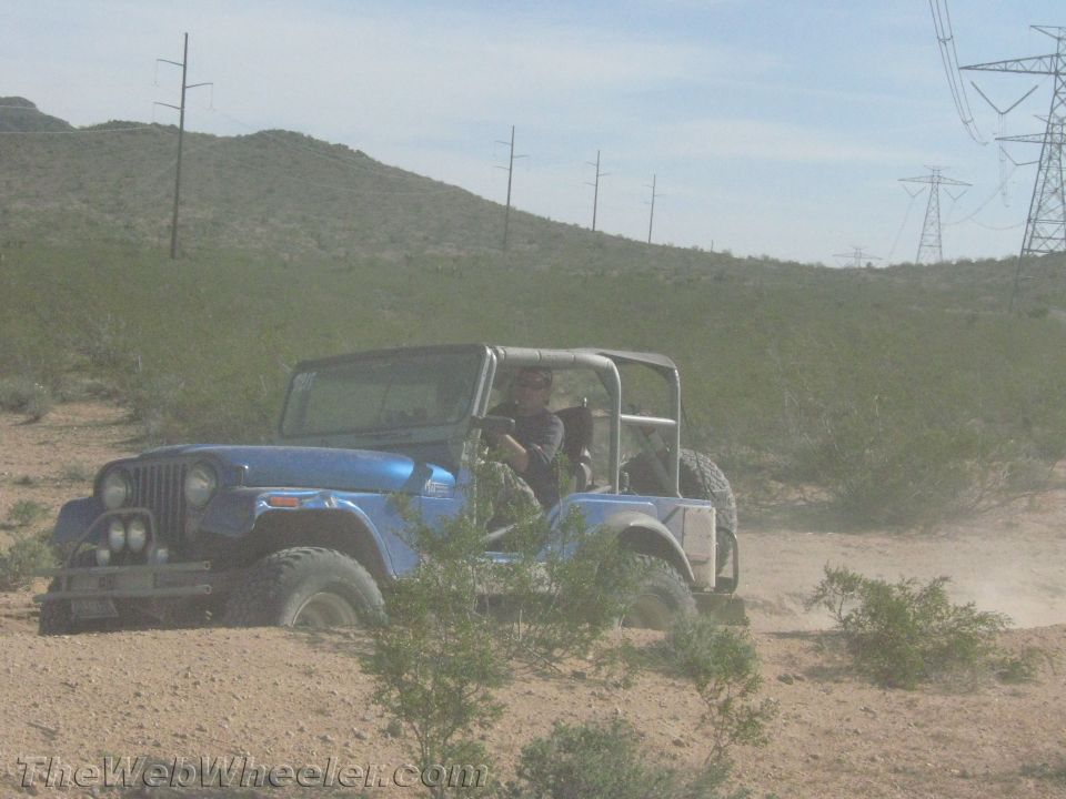 Blue Jeep CJ on off-road tires driving through desert scrub