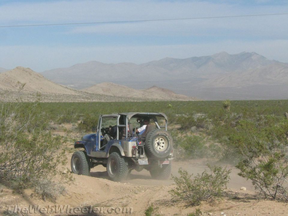 Blue Jeep CJ with rear spare driving a desert trail