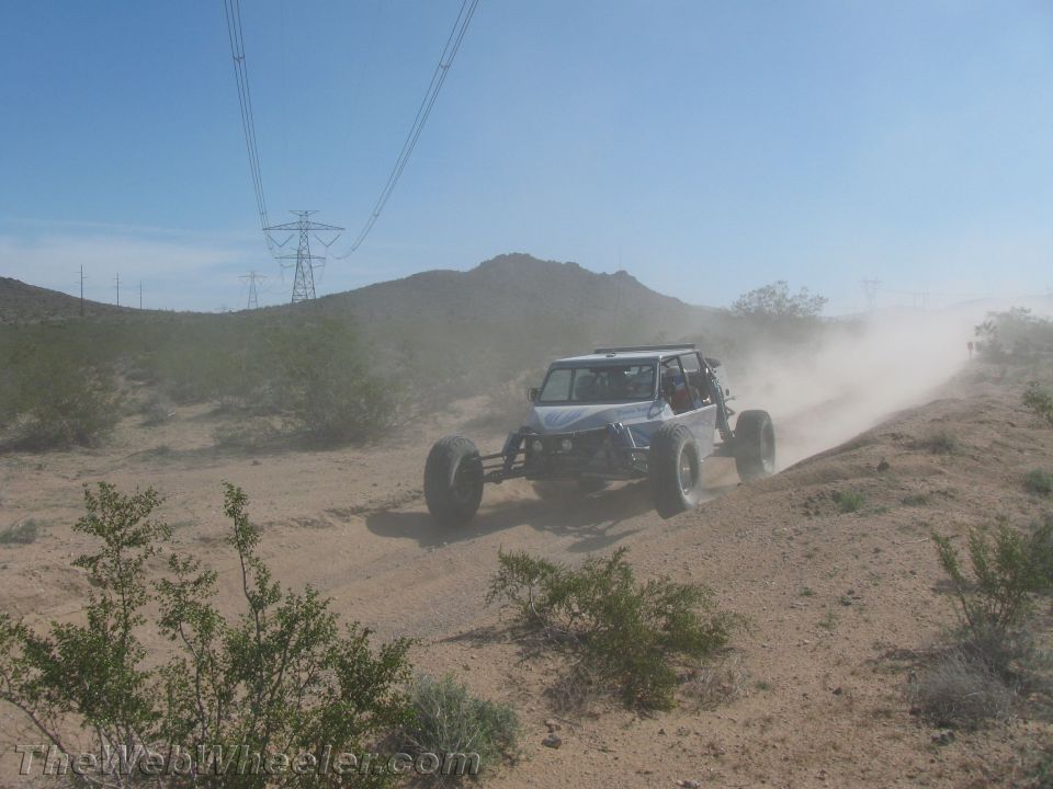 White off-road buggy climbing a dusty desert berm