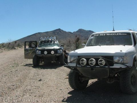 1990 Ford Bronco - white off-road SUV lettered TheWebWheeler.com is parked beside a dark Jeep on a desert trail.