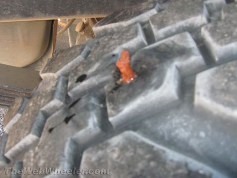 1990 Ford Bronco - Close-up of a chunky off-road tire tread with a small orange object stuck between the blocks under a vehicle.