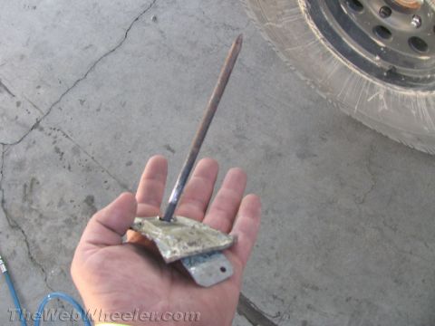 1990 Ford Bronco - person holds a flat metal bracket with a long spike in their palm over a concrete floor beside a tire.