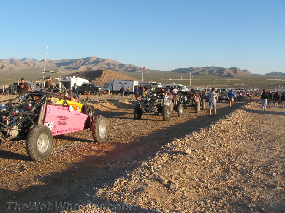 Pink off-road buggy and other race cars lined up at a desert staging area