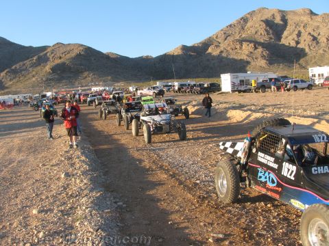 1990 Ford Bronco - long line of single-seat off-road race buggies, including number 1622, waits on a gravel road at a desert race event.