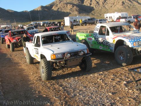 1990 Ford Bronco - white truck numbered 351, a red truck and a stars-and-stripes truck numbered 850 are staged on gravel at a desert event.