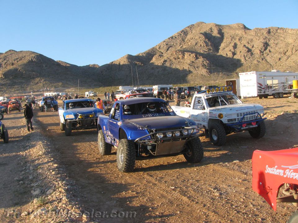 Blue, white and other off-road race trucks staged in a desert pit