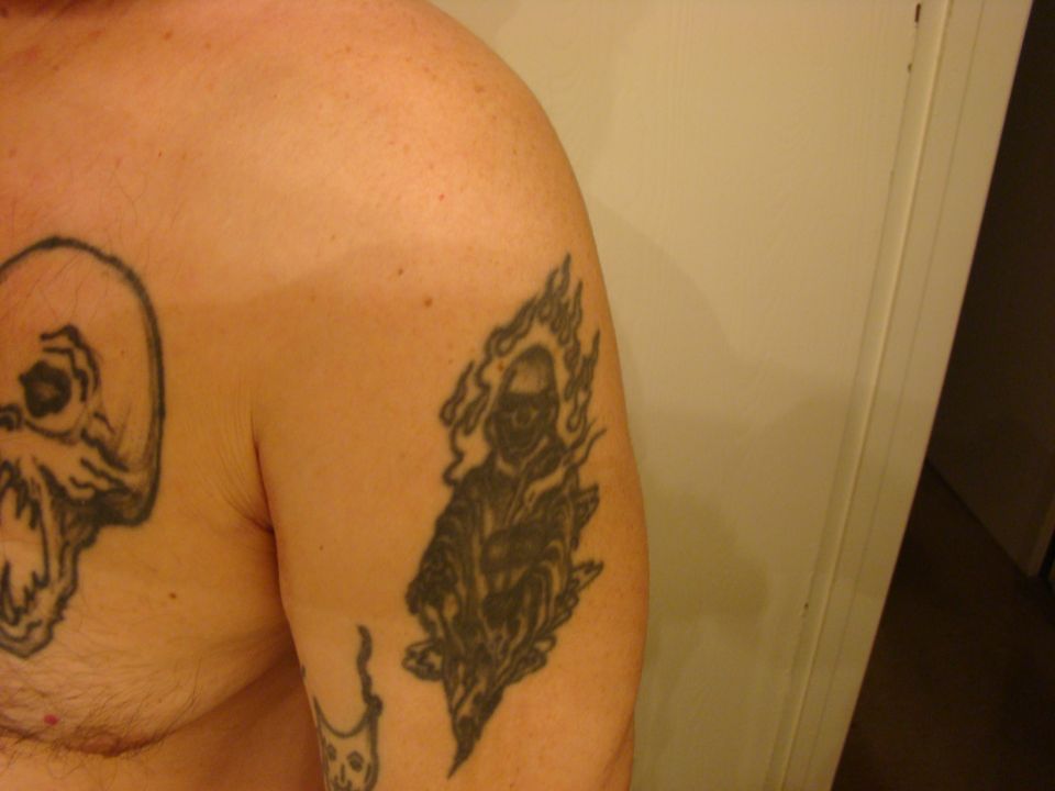 Close-up of shoulder and chest tattoos including a skull and flaming skeleton rider