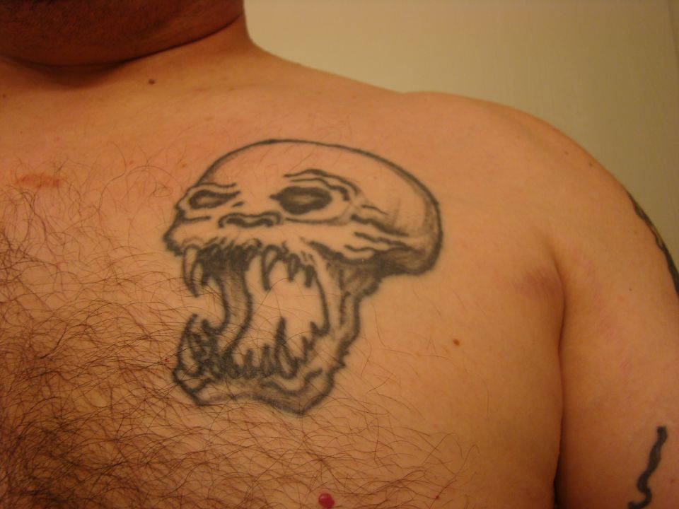 Tattoo of a skull with fangs on a hairy chest