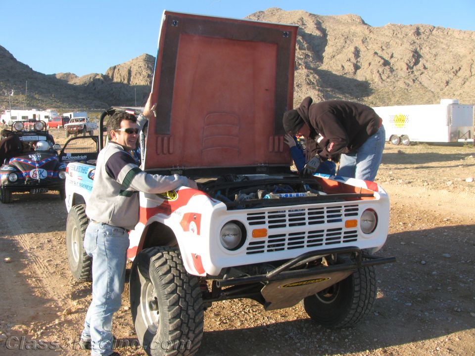 Crew working on white off-road Bronco with hood open in desert pits