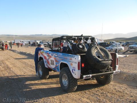 1990 Ford Bronco - Rear view of a red-white-and-blue early Ford Bronco off-road racer number 304 with spare tire, staged on a desert course.