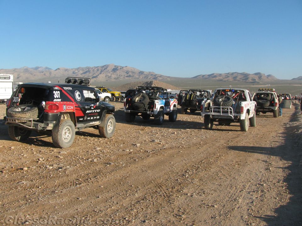 Row of off-road race trucks staged along desert trail under blue sky
