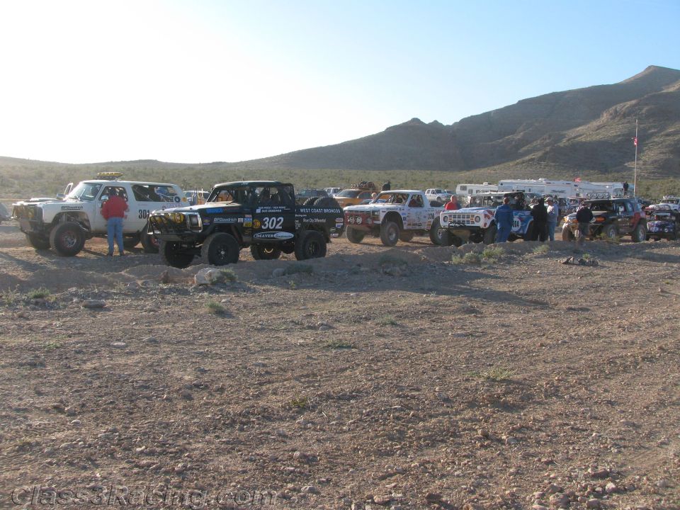 Line of off-road race trucks staged in desert led by number 302
