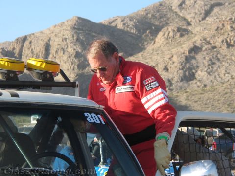 1990 Ford Bronco - man in a red BFGoodrich racing suit leans in to climb into the caged cab of number 301 race truck in the desert.